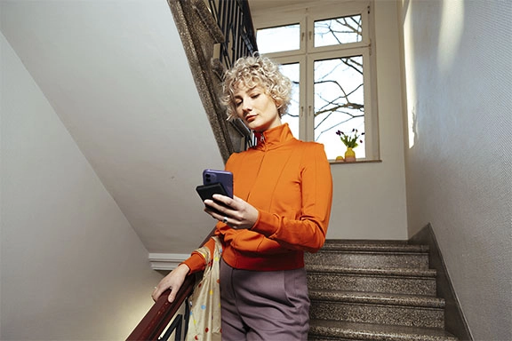 Woman walks down the stairs, her mobile phone is being charged via a power bank.