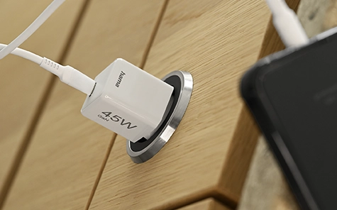 45 watt charger is plugged into a socket in a wooden wall and charges a smartphone.