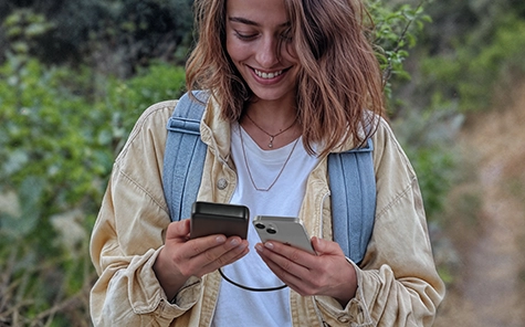 A young woman is hiking and conveniently charges her smartphone with the Hama Power Pack