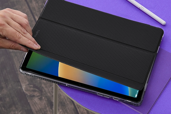 The Apple iPad 10.9’ is in the Hama “Extreme Protect” tablet sleeve and is lying on a table with a purple surface. One hand grips the cover from the left and opens the iPad. This automatically activates the screen.