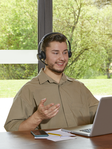 Person is sitting at the table and happily talking on a laptop using the wireless office headset.