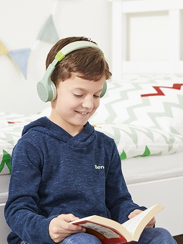 A boy sits in his room and reads a book while wearing the Hama Bluetooth® headphones "Teens Guard"