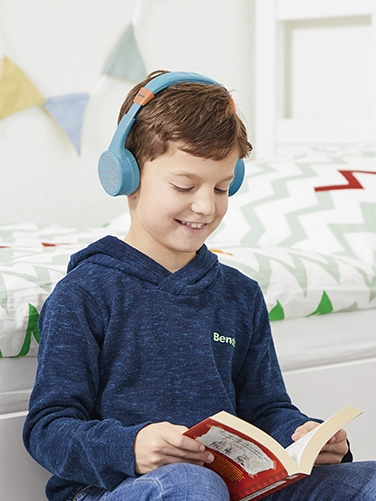 A boy sits in his room and reads a book while wearing the Hama Bluetooth® headphones "Teens Guard II"