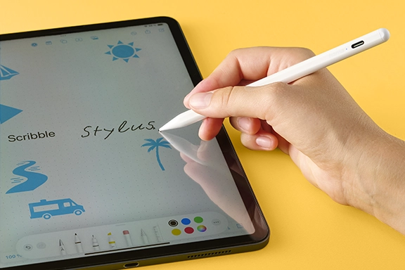 A tablet with an open drawing programme lies on a yellow background. One hand holds the Hama tablet pen ‘Scribble’ and operates the drawing app