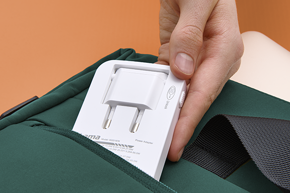 The network plug of the Hama quick charger can be folded in so that it can be stowed away to save even more space. In the picture, it is being put into a green rucksack by one hand.