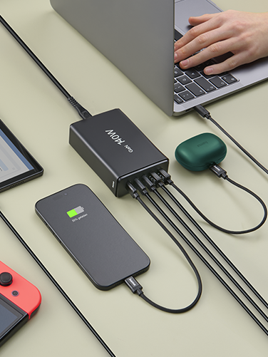 An open laptop, tablet, smartphone, Nintendo Switch and Bluetooth headphones are lying on a table. They are all charged simultaneously via the Hama charging station.