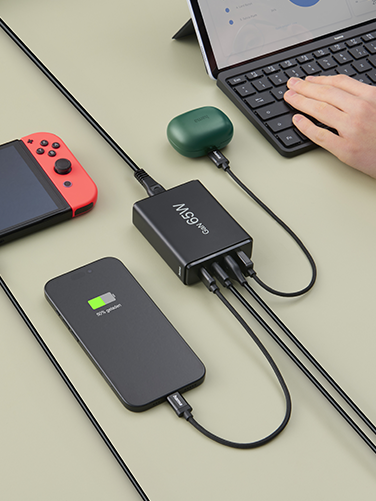 An open laptop, smartphone, Nintendo Switch and Bluetooth headphones are lying on a table. They are all charged simultaneously via the Hama charging station.