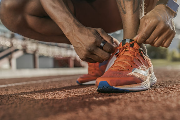 A person tying their running shoes on a running track, with a smart ring visible on their finger; fitness, sport, modern wearable design