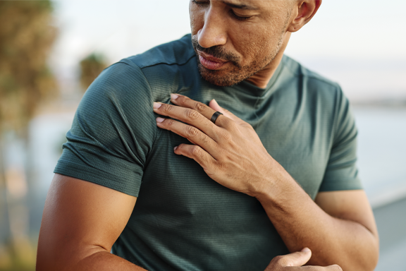 Man touching his shoulder; smart ring visible on his finger; outdoors; sleek design; high-quality wearable accessory
