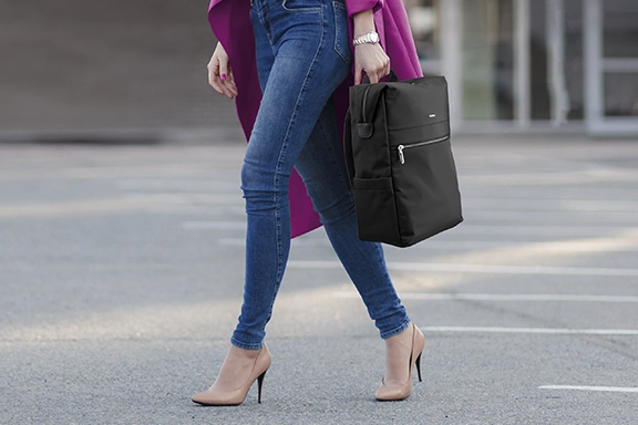 A woman in a striking pink parka carries the ‘Ultimate’ laptop rucksack loosely as a briefcase by the handles across a car park